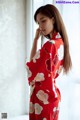 A woman in a red kimono standing by a window.