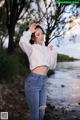 A woman in a white shirt and jeans standing by a river.