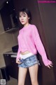 A woman in a pink sweater and denim shorts posing for a picture.