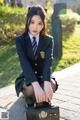 A woman in a school uniform sitting on a suitcase.