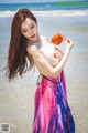 A woman in a colorful dress holding a leaf on the beach.