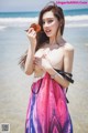 A woman in a colorful dress holding a leaf on the beach.