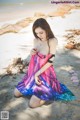 A woman in a colorful dress sitting on the beach.