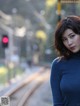 A woman in a blue turtle neck sweater standing on a train track.