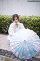 A woman in a blue kimono sitting on the ground holding an umbrella.