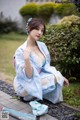 A woman in a blue kimono sitting on the ground with an umbrella.