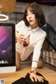 A woman in a white shirt is sitting on a desk with a computer.