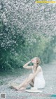 A woman sitting on the ground in front of a flowering tree.