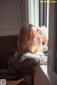 A woman looking out of a window with her hand on her head.