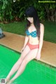 A woman in a bikini sitting on the edge of a pool.