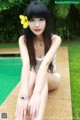 A woman sitting on the edge of a swimming pool with a flower in her hair.