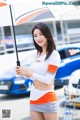 A woman holding an umbrella standing in front of a car.