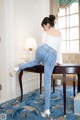 A woman in a white top and blue jeans leaning on a table.