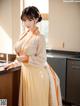 A woman in a yellow and white dress standing in a kitchen.